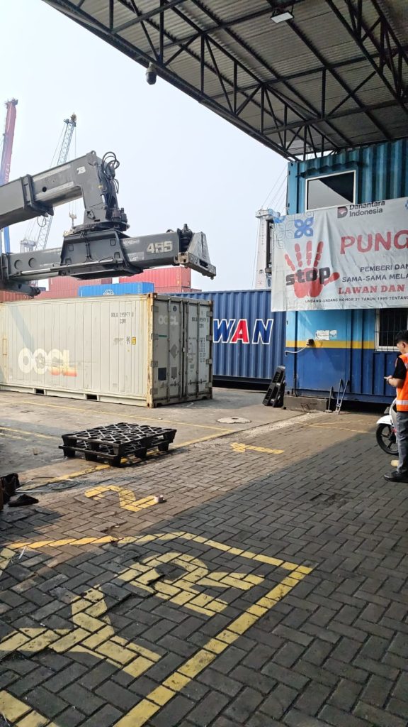 Alat berat reach stacker memuat kontainer ke atas armada truk logistik USLOGT di area depo
